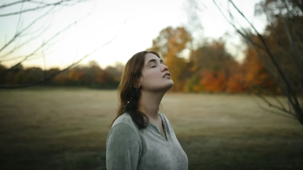 Femme respirant les yeux fermés dans un champ, lumière naturelle
